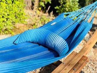 Coussin cervical en tissu rayé bleu et blanc, en forme de demi-lune, posé sur un hamac bleu dans un environnement extérieur