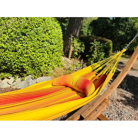 Coussin sur un hamac en tissu à rayures rouges et jaunes est suspendu dans un jardin