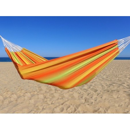 Hamac coloré en coton aux rayures orange, jaunes et vertes, installé sur une plage ensoleillée avec ciel bleu éclatant