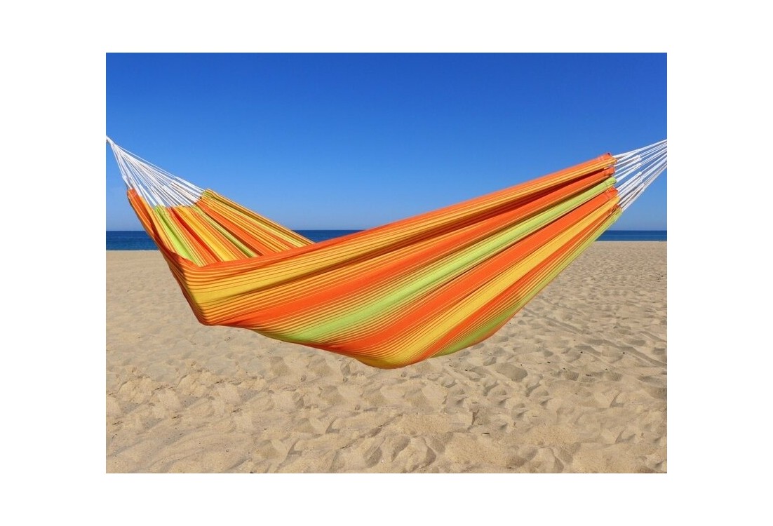 Hamac coloré en coton aux rayures orange, jaunes et vertes, installé sur une plage ensoleillée avec ciel bleu éclatant