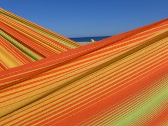 Zoom sur le tissu d’un hamac artisanal aux rayures orange, jaunes et vertes, soulignant la qualité du tissage en coton