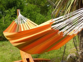 Hamac rayé multicolore suspendu sur un support en bois dans un jardin verdoyant, parfait pour la détente en plein air