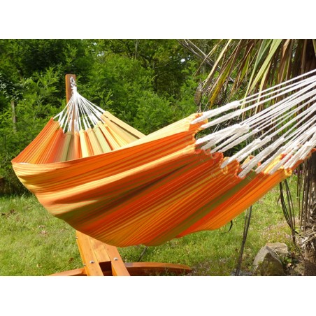 Hamac rayé multicolore suspendu sur un support en bois dans un jardin verdoyant, parfait pour la détente en plein air