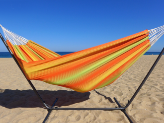 Hamac à rayures aux tons chauds installé sur un support métallique dans le sable de la mer