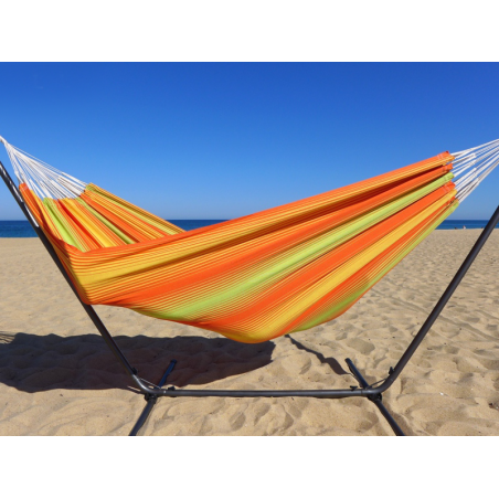 Hamac à rayures aux tons chauds installé sur un support métallique dans le sable de la mer