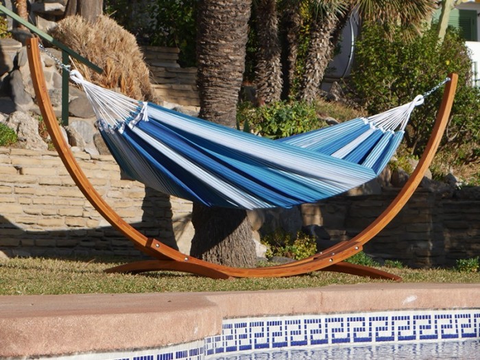 Hamac XXL rayé bleu et blanc avec support en bois suspendu dans un jardin avec des palmiers