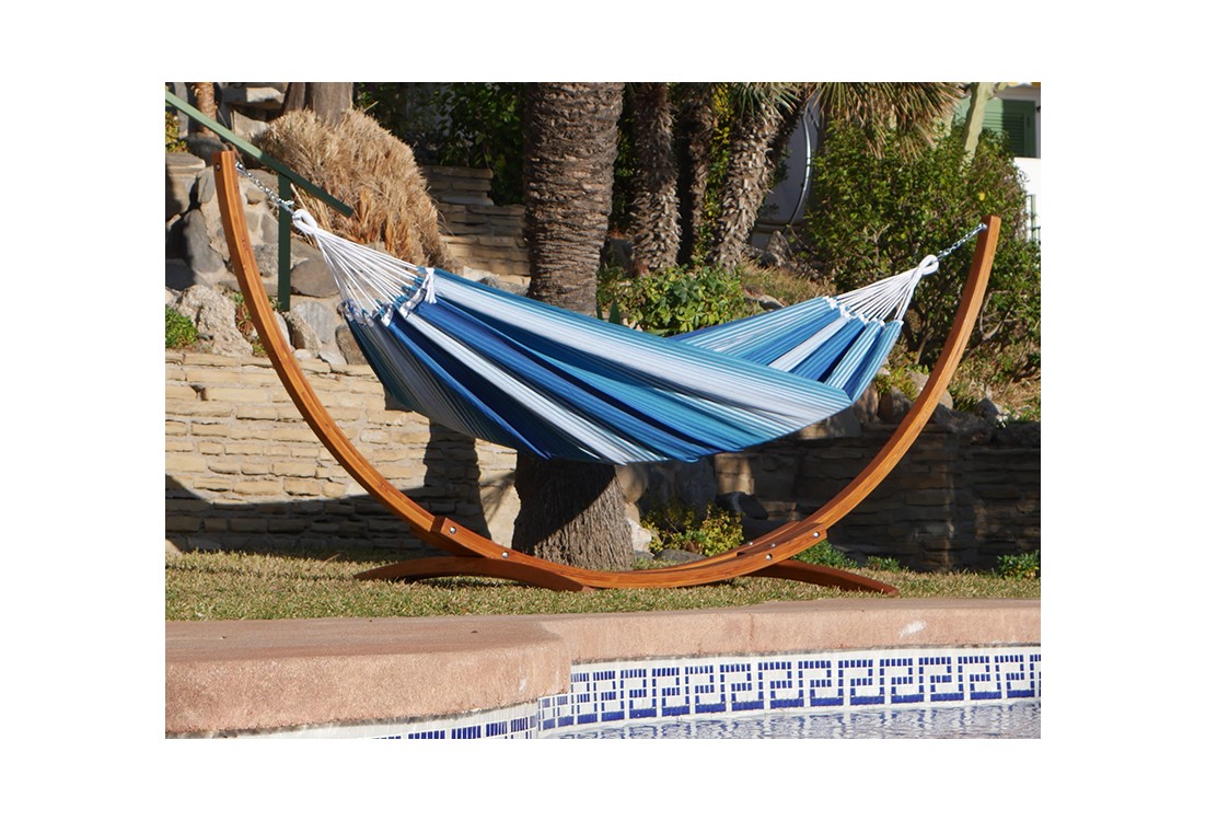 Hamac XXL rayé bleu et blanc avec support en bois suspendu dans un jardin avec des palmiers