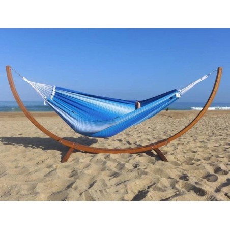 Hamac rayé bleu et blanc avec support en bois sur une plage de sable doré