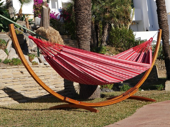 Un hamac poligono rouge et blanc suspendu à un support en bois dans un décor de jardin