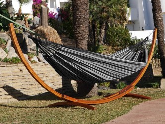 Hamac polygone noir XL avec support en bois, situé dans un jardin ensoleillé