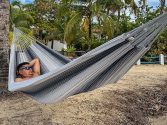 Hamac artisanal colombien en coton recyclé, tons gris et noir, suspendu entre deux arbres – confort et authenticité.