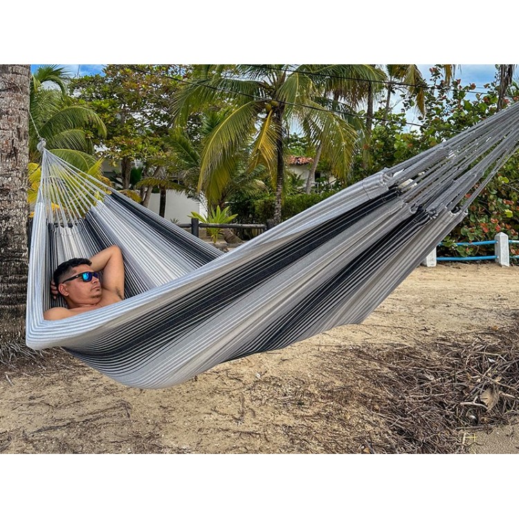 Hamac artisanal colombien en coton recyclé, tons gris et noir, suspendu entre deux arbres – confort et authenticité.