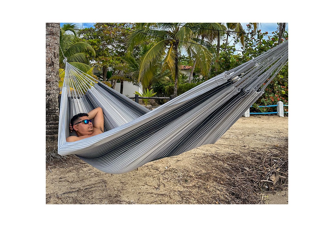 Hamac artisanal colombien en coton recyclé, tons gris et noir, suspendu entre deux arbres – confort et authenticité.
