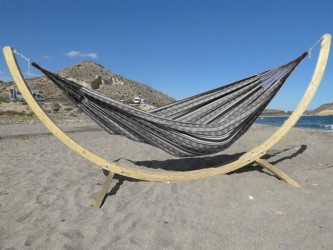 Hamac colombien à rayures noires et blanches sur un support en bois incurvé, au bord de la mer