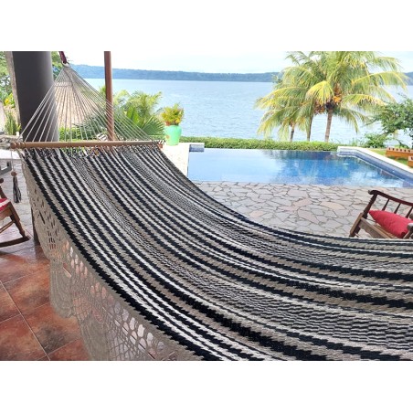 Hamac artisanal à barre, noir et écru suspendu dans un jardin tropical, parfait pour se relaxer au bord de la piscine