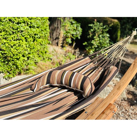 Coussin sur un hamac en tissu à rayures marron et blanches est suspendu dans un jardin