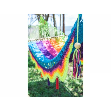 Hamac coloré arc-en-ciel, prêt à l'emploi, installé entre deux arbres avec un paysage naturel en arrière-plan