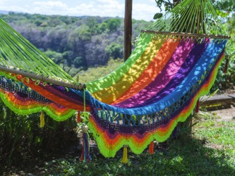 Hamac artisanal aux couleurs vives et motif arc-en-ciel, suspendu entre des palmiers dans un environnement tropical