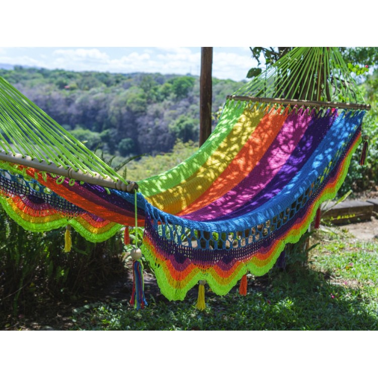 Hamac artisanal aux couleurs vives et motif arc-en-ciel, suspendu entre des palmiers dans un environnement tropical