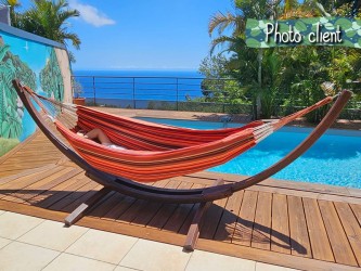 Photo d'un client profitant d'un hamac à rayures rouges sur un support en bois, au bord d'une piscine