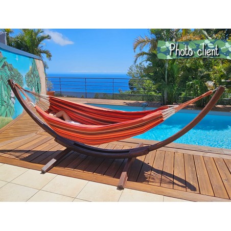 Photo d'un client profitant d'un hamac à rayures rouges sur un support en bois, au bord d'une piscine