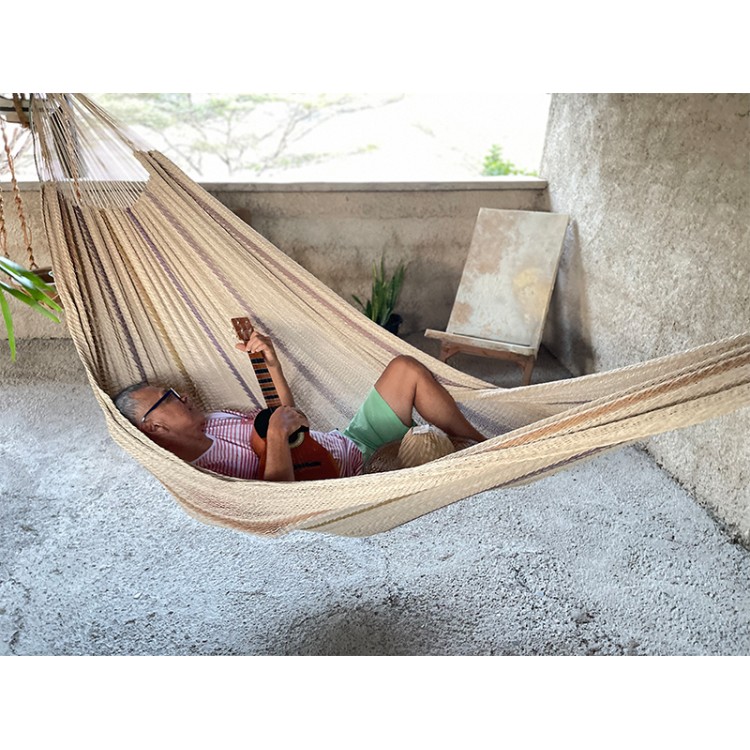 Homme allongé dans un hamac Moriche à rayures marron sur une terrasse rustique