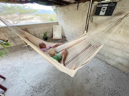 Homme allongé dans un hamac Moriche à rayures rouges et bleues sur une terrasse rustique