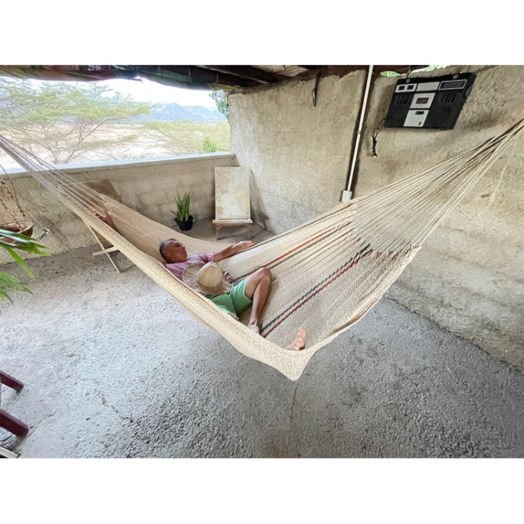 Homme allongé dans un hamac Moriche à rayures rouges et bleues sur une terrasse rustique