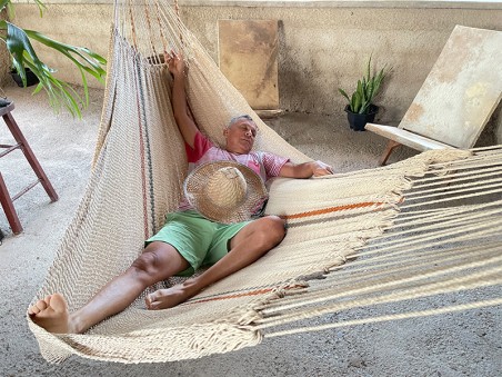 Homme allongé dans un hamac Moriche à rayures rouges et bleues sur une terrasse rustique
