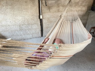 Homme allongé dans un hamac Moriche à rayures rouges et bleues sur une terrasse rustique