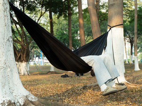 Vue latérale d'une personne se reposant dans le hamac ultra léger noir, installé entre deux troncs d'arbres en extérieur