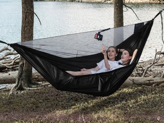 Hamac noir avec moustiquaire intégrée installé entre les arbres au bord du lac