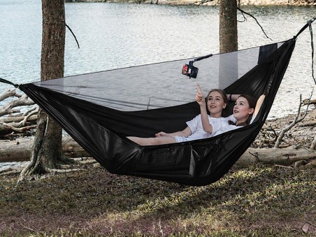 Hamac noir avec moustiquaire intégrée installé entre les arbres au bord du lac