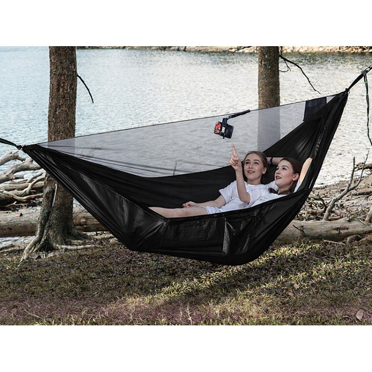 Hamac noir avec moustiquaire intégrée installé entre les arbres au bord du lac