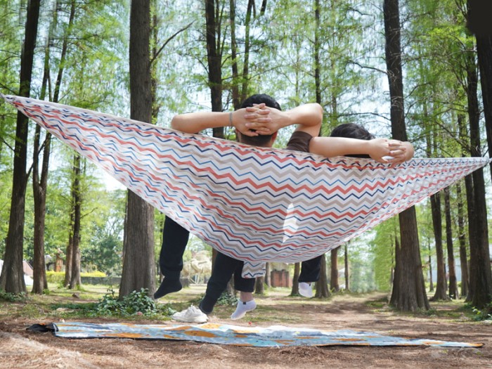 Deux personnes détendues dans un hamac explorer L nylon blanc suspendu entre deux arbres, avec une couverture au sol