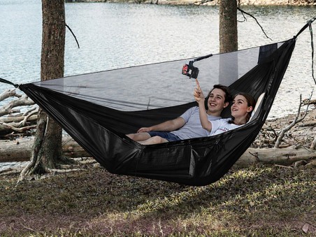 Hamac noir avec moustiquaire intégrée installé entre les arbres au bord du lac