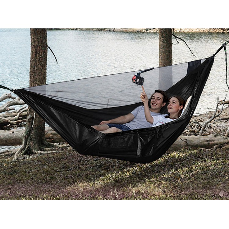 Hamac noir avec moustiquaire intégrée installé entre les arbres au bord du lac