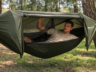 Garçon utilisant un hamac de survie avec moustiquaire et bâche anti-pluie intégrée dans la nature pour se reposer