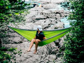 Femme assise dans un hamac outdoor flex XL Vert et gris suspendu au milieu d'une cascade en pleine nature