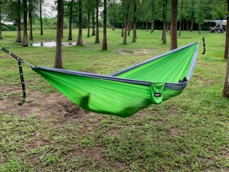 Un homme allongé dans un hamac outdoor flex XL Vert et gris au milieu de la forêt, entre les arbres