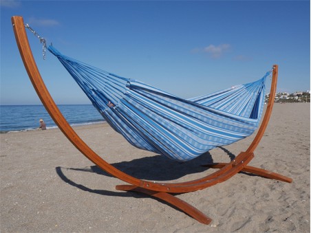 Hamac colombien à rayures turquoises et blanches sur un support en bois incurvé, au bord de la mer