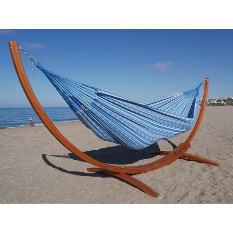 Hamac colombien à rayures turquoises et blanches sur un support en bois incurvé, au bord de la mer