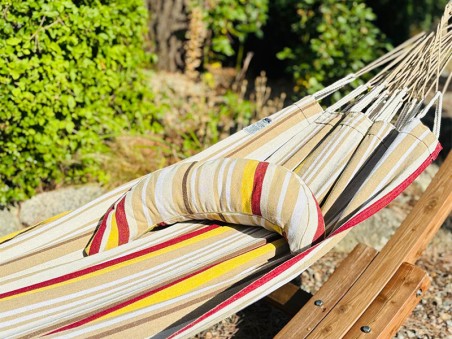 Coussin sur un hamac en tissu à rayures beiges, grenat, ocre et blanc est suspendu dans un jardin