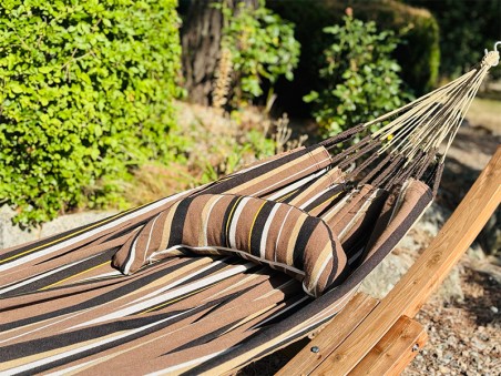 Coussin sur un hamac en tissu à rayures marron, blanc, jaune et noir est suspendu dans un jardin